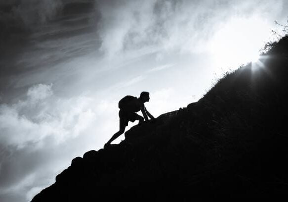 Black and white image of man climbing up a mountain.